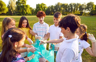 Group of a young teenage happy smiling volunteers children standing in a row in gloves and with garbage bags collecting trash in the summer park outdoors. Cleaning environmental pollution by garbage.