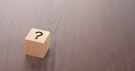 one wooden block with question mark over a brown background with copy space