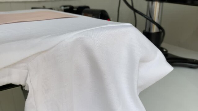 Male hand applying pressure on white T shirt heat press printing machine close up view.