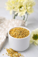 Fresh bee pollen granules and flowers on white tiled table, closeup