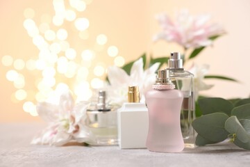 Bouquet of beautiful lily flowers and perfume bottles on table against beige background with blurred lights, closeup. Space for text