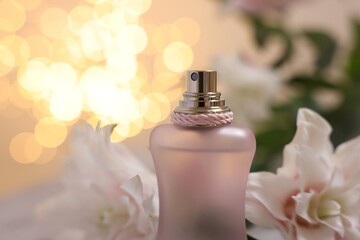 Bottle of perfume and beautiful lily flowers against beige background with blurred lights, closeup