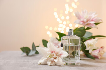 Obraz na płótnie Canvas Bottle of perfume and beautiful lily flowers on table against beige background with blurred lights, space for text