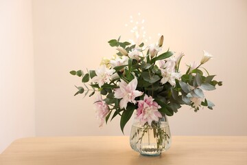 Bouquet of beautiful lily flowers in vase on wooden table against beige background