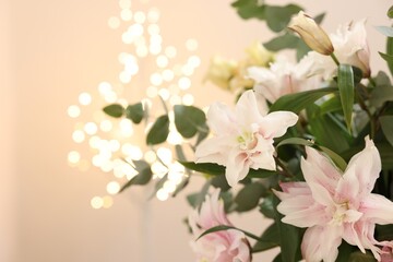 Bouquet of beautiful lily flowers against beige background with blurred lights, closeup. Space for text