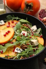 Tasty salad with persimmon, blue cheese, pomegranate and walnuts served on wooden table, closeup