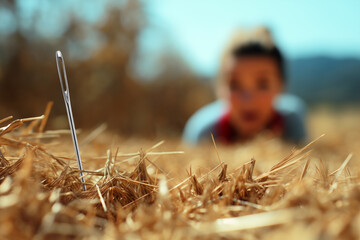 Close-up of a needle in a haystack with a blurred background of a person looking for it with a satisfied face. "it's harder than finding a needle in a haystack."