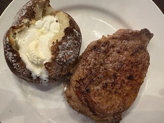 A medium rare ribeye steak paired with a baked potato topped with butter and sour cream