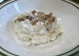 A scoop of cottage cheese sprinkle with ground pepper in a white bowl