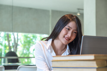 university library beautiful smart student talking on online. Young asian student adult smiling wearing write to paper. happy at the college desk laptop on the table,girl chat meeting campus at office