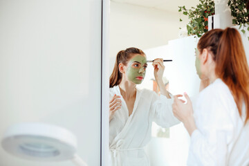 Young woman applying clay mask on face