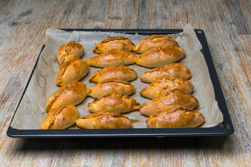 mini pies Pirozhki or piroshki on a cooking tray. Homemade baked yeast boat shaped buns with cabbage fillings. Eastern Europe food.