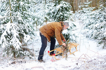 a man stacks firewood on a sled in the winter forest