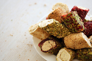 Many rolls of turkish delight with different flavors and fillings in white plate on table. Cuts of Turk Lokumu sweets