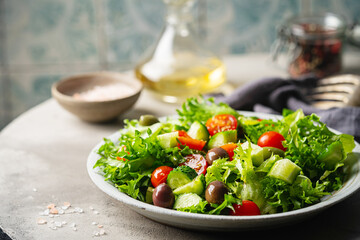 Classic vegetable salad with fresh olives, tomatoes, cucumbers and olive oil on gray background.