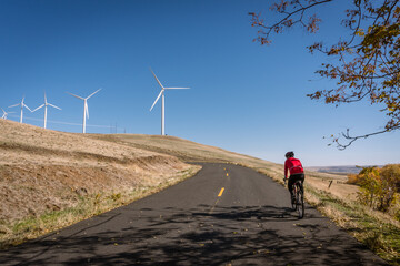 Man bicycling on road with wind turbines in background.