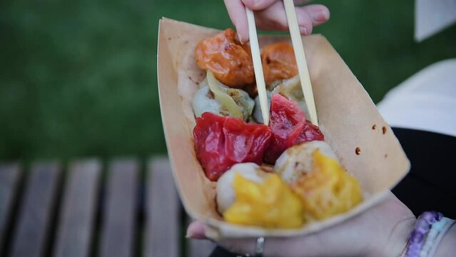 Hand of woman holding bamboo chopsticks and eating colorful dumplings from craft plate, take away food