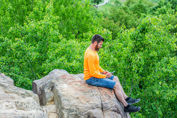 Man sitting on a edge of a cliff and looking at beautiful and rough terrain around him. Active...