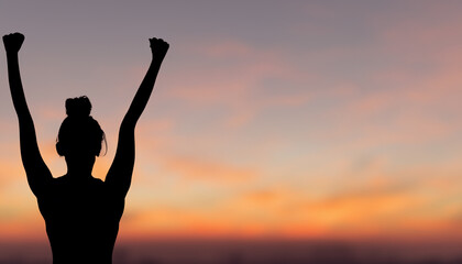 Fototapeta premium A silhouette of a woman raising her fist in the air with a sunset background