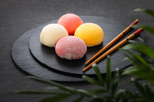 Four round multi-colored mochi lie on black slate. Dark background with leaves and sticks. Perfect retouching. Advertising. View from above. Photo