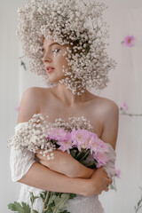 Portrait of sensual blond woman with flowers. Beautiful girl with flowers in her hair. Summer Beauty. Art in a contemporary style. A gypsophila wreath on a white background. Perfume, cosmetics concept