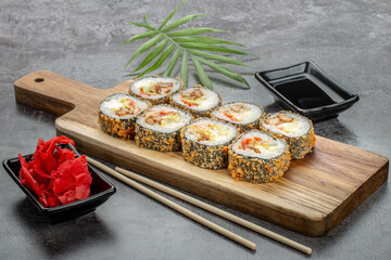 Hot rolls in batter with seafood, salad and cream cheese on a gray background, next to ginger, soy sauce and bamboo sticks. Top and side view. Photo