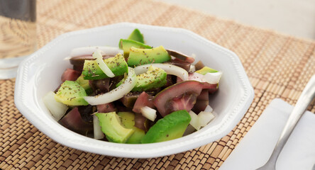 Salad of black tomatoes, avocado and onions in white ceramic bowl