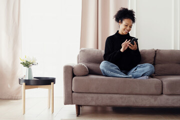Smiling woman using smartphone comfortably at home, epitomizing relaxed technology use and modern connectivity.