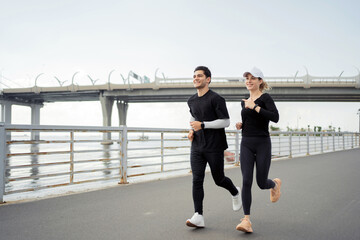 Happy couple jogging together on a waterfront promenade, enjoying a healthy lifestyle.