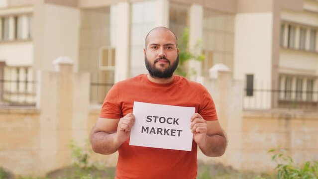 Bald indian Man Holding Stock Market Poster