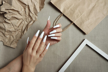 The extension of long white nails on a background with paper objects.