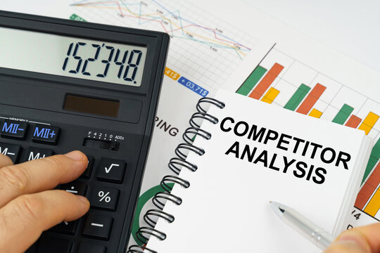 On the table there is a calculator, reports with graphs and a notepad with the inscription - Competitor Analysis
