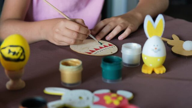 Close-up of little girl painting wooden egg at table, making Easter decorations at home