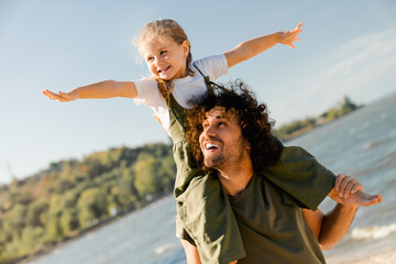 Caucasian loving father with happy daughter on shoulders walking on the beach