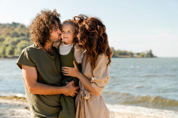 Image of young happy family kissing their daughter outdoors at the beach
