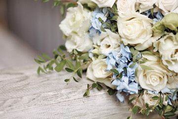 An elegant bouquet with blooming white roses and delicate blue flowers rests on a wooden railing....