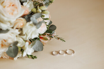 Elegant wedding rings lay near a lush bouquet on a soft beige surface, capturing the essence of matrimonial bliss. Concept for wedding planners or romantic events.
