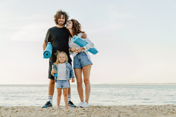 Full length portrait of happy family on beach with yoga mat and water bottle in hands.