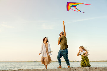 Young father and mother with daughter child kid playing outside with flying kite together