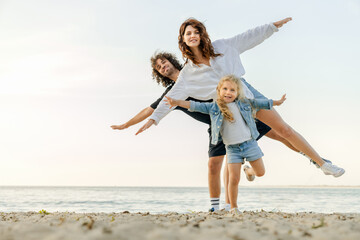 Young happy family having fun while doing yoga exercises on sunny beach.