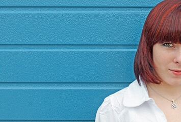 Naklejka premium Gesichtshälfte von einer jungen rothaarigen Frau vor einem blauen Tor