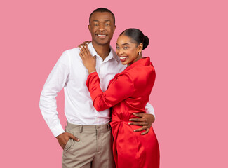 Smiling black couple embracing, woman in red dress, man in white shirt, pink background