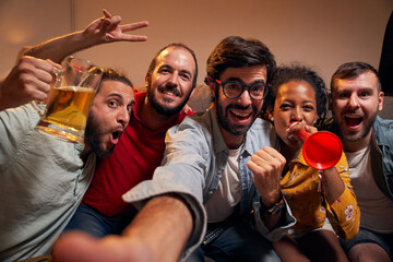 Selfie portrait looking at camera of group handsome Caucasian friendly women watching football game on TV while sitting on sofa at night. Friends looking at camera POV sport channel late in evening. - obrazy, fototapety, plakaty