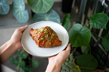 Woman hand holding plates with fresh garlic butter croissant with green plant background