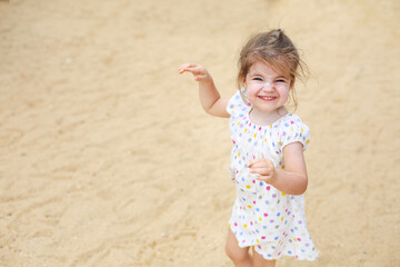 Cute blond baby girl in beautiful dress walking on a long sandy beach