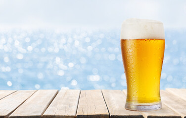 glass of beer on wooden table on sea background