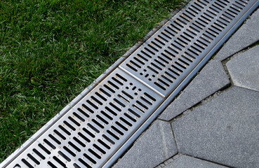 iron grate of a drainage system for storm water drainage from a pedestrian sidewalk near a green...