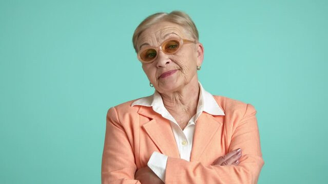 Medium shot of old woman with short haircut in business outfit standing on aquamarine background, looking with disgust. Arrogant dissatisfied elderly lady. High quality 4k footage