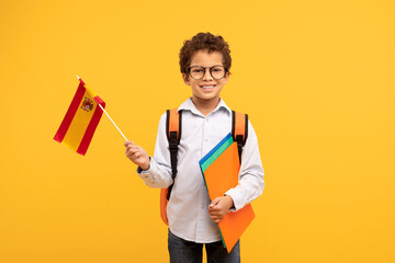 Smiling boy with Spanish flag and school folders, bright yellow bacdrop