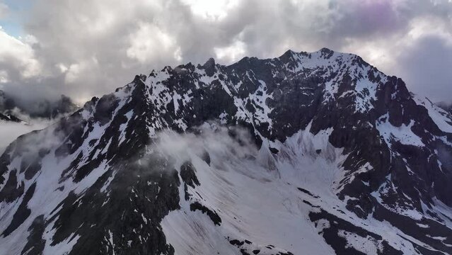 aerial view flying over a mountain range in front of a high rocky mountain peak at sunset. High contrast, stabilized footage shot from the air. Mountains in early spring